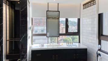 A modern bathroom with a large mirror, a sink with toiletries, and a view of buildings through a window.