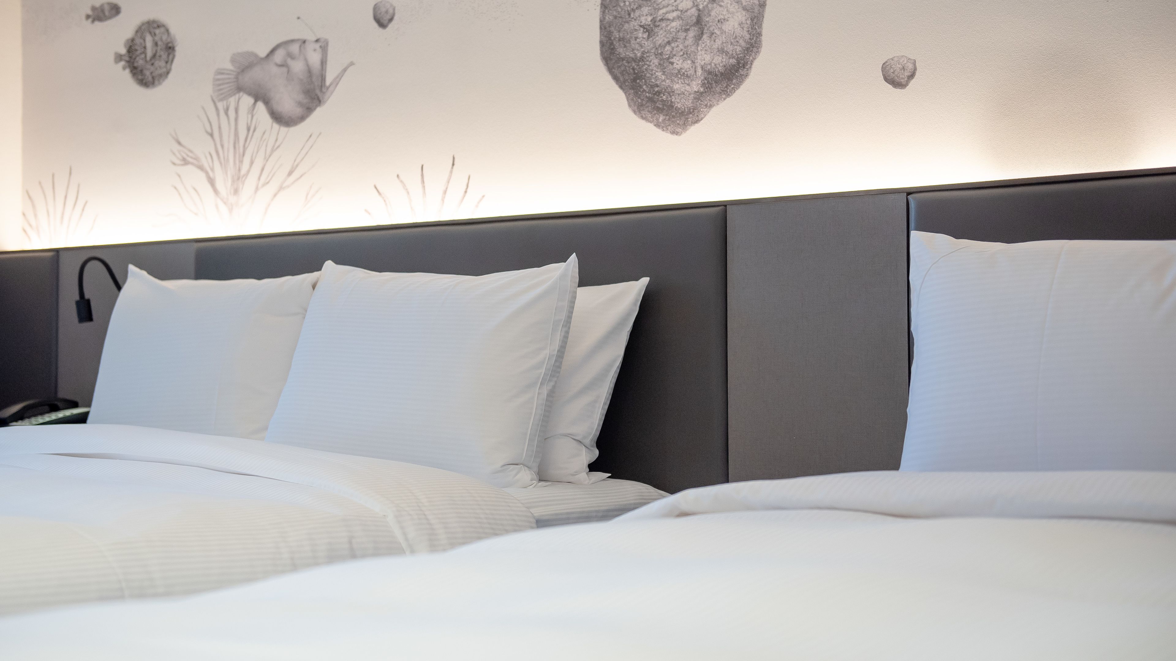 A hotel room with a bed, pillows, and a wall mural.