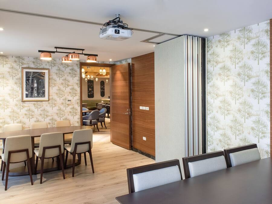 A conference room with a wooden table and chairs, a projector, and a patterned wallpaper.