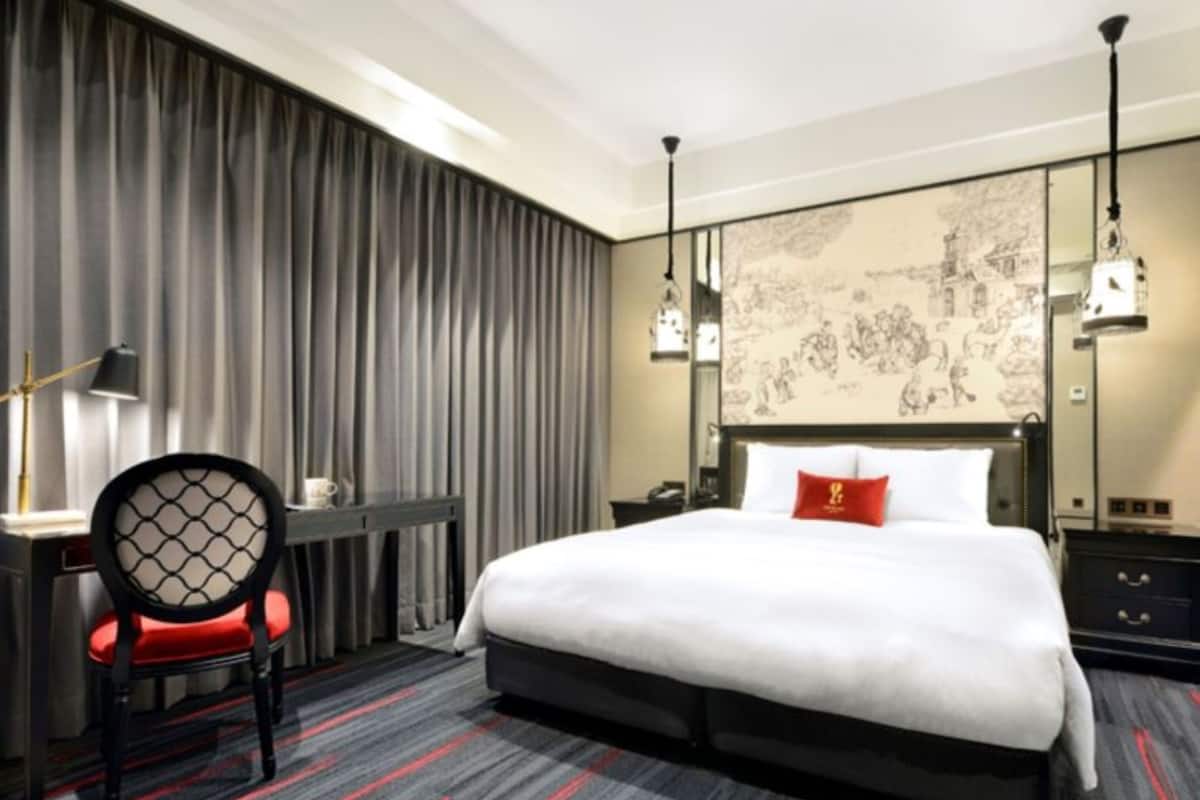 A hotel room with a large bed, a desk with a chair, a lamp, and a wall with a map.