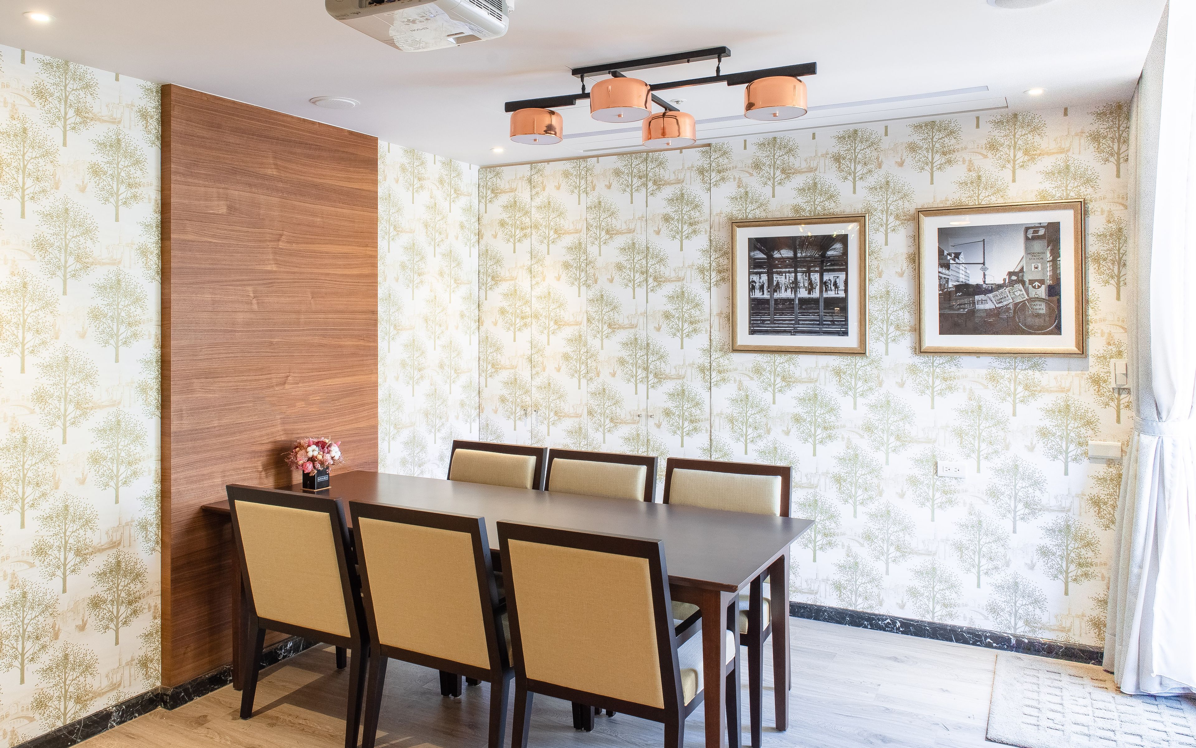 A dining area with a long table, six chairs, and framed pictures on the wall.