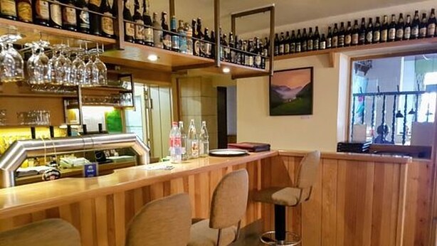 A bar area with wooden bar stools, shelves of bottles, and glasses. - Heide Hotel Klütz (Burgwedel)