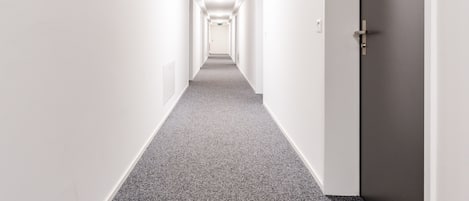 Un pasillo largo y estrecho con paredes blancas y alfombra gris.