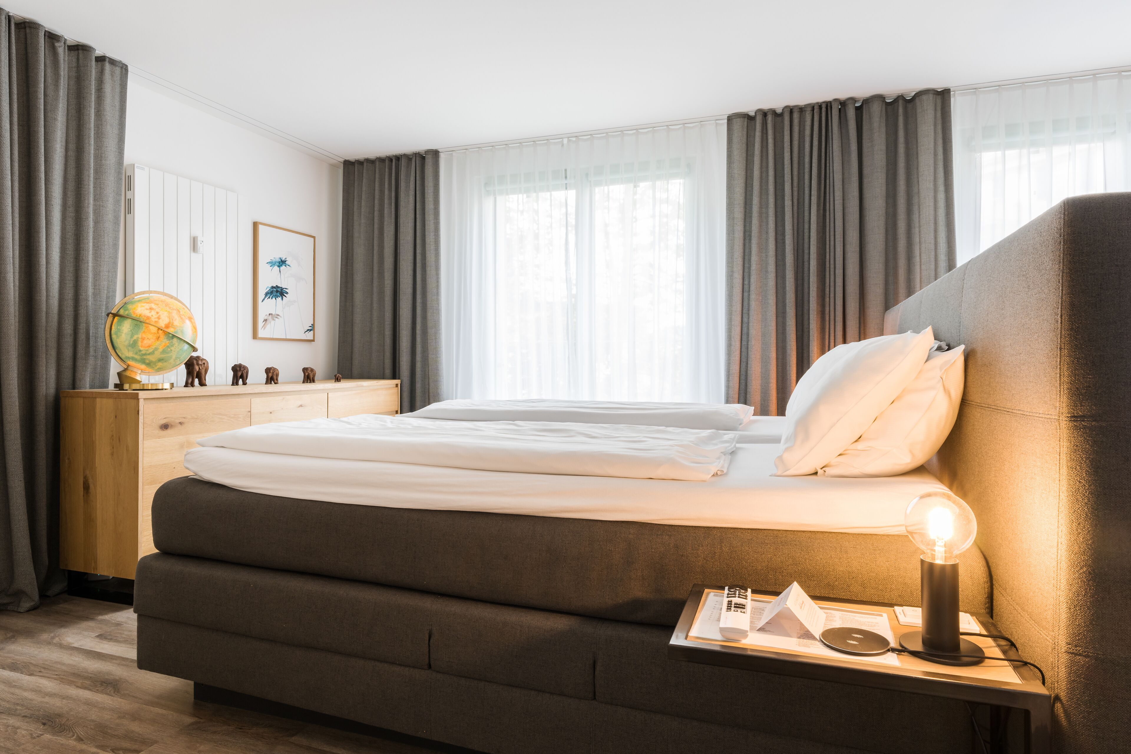 A neatly made bed with white linens, a bedside lamp, and a wooden nightstand with a globe and small figurines.
