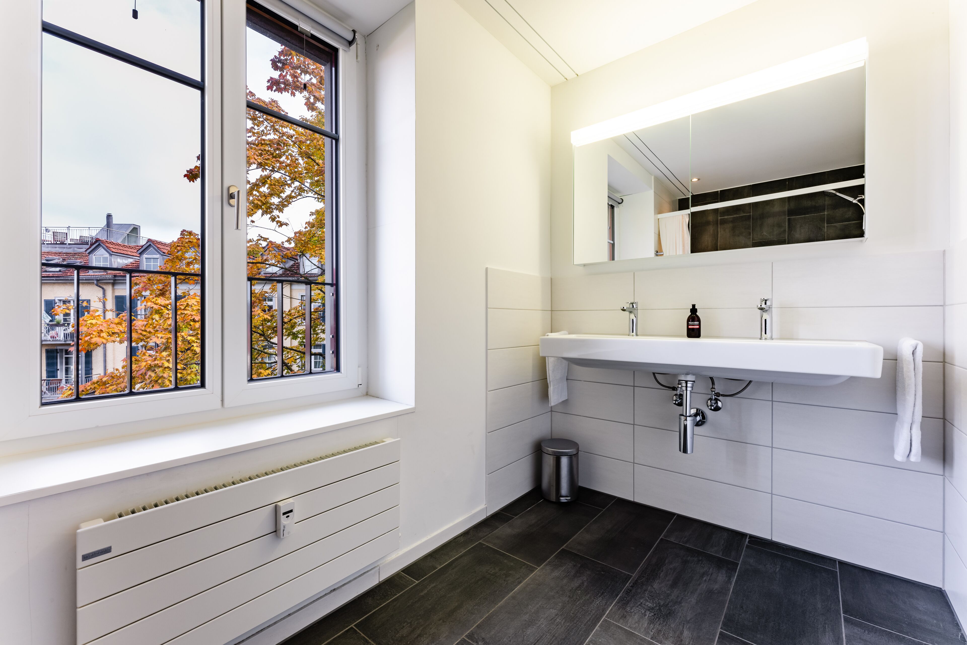 A modern bathroom with a large window, a white sink, and a mirror above it.