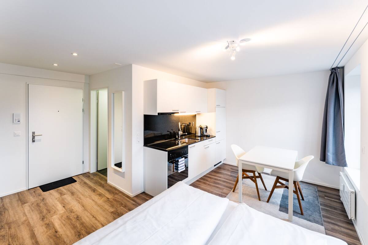 Habitació d'hotel moderna amb terra de fusta, un llit, una cuineta petita i zona de menjador.