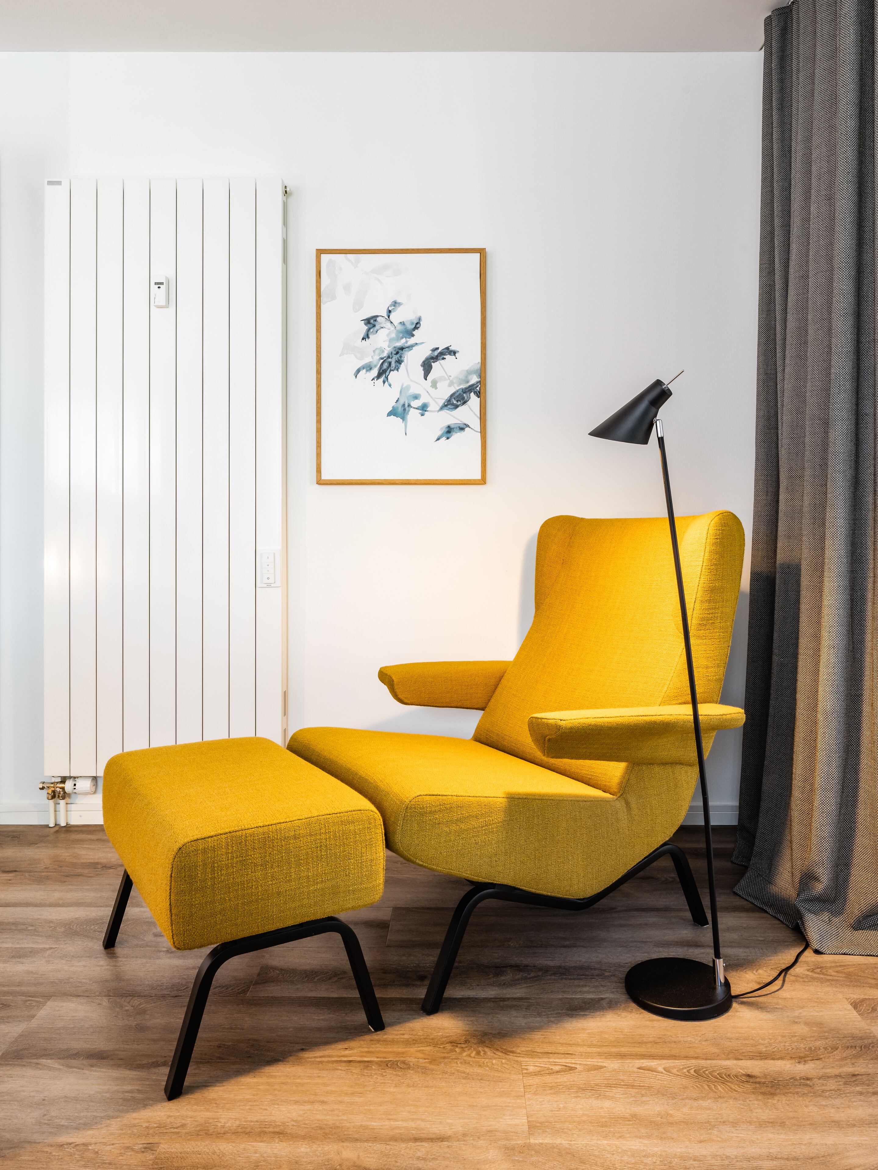 A modern living room with a mustard yellow armchair, a black floor lamp, and a framed abstract painting on the wall.