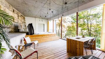 A wooden deck with a dining table and chairs, a hot tub, and a stone wall.
