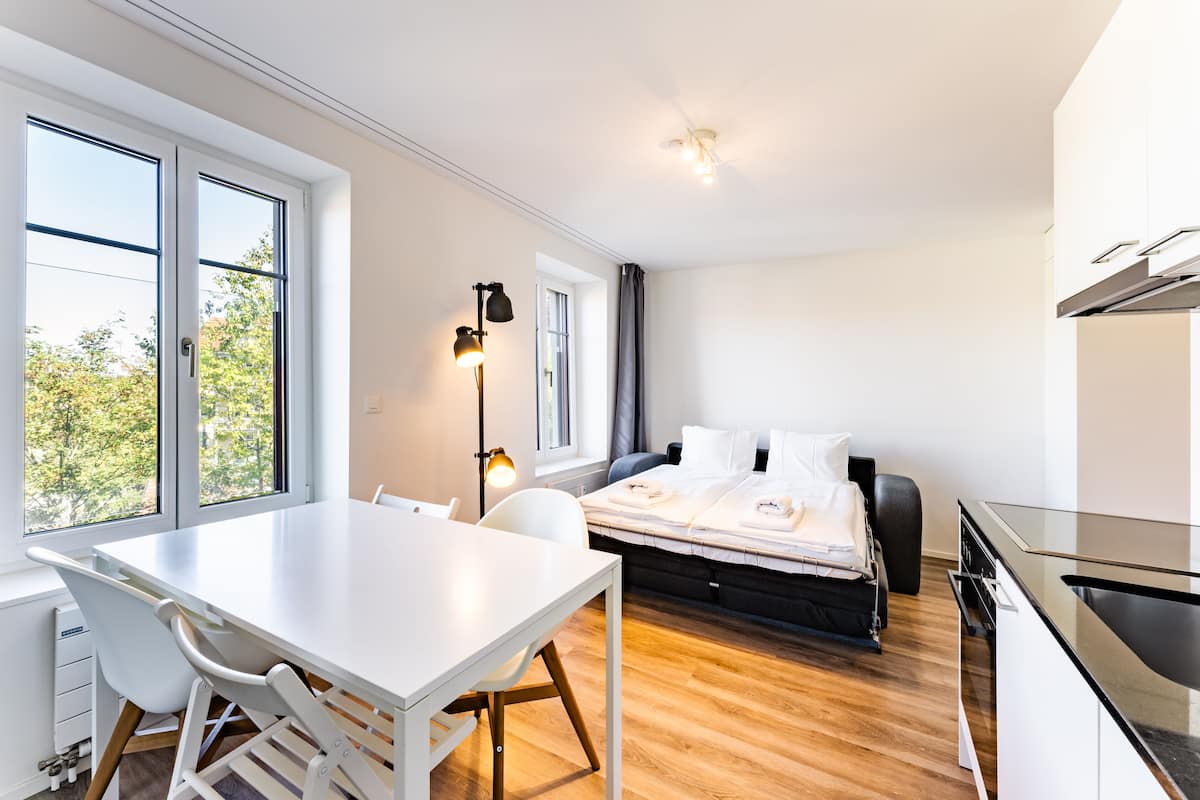 Habitació moderna amb llit, taula de menjador i zona de cuina.