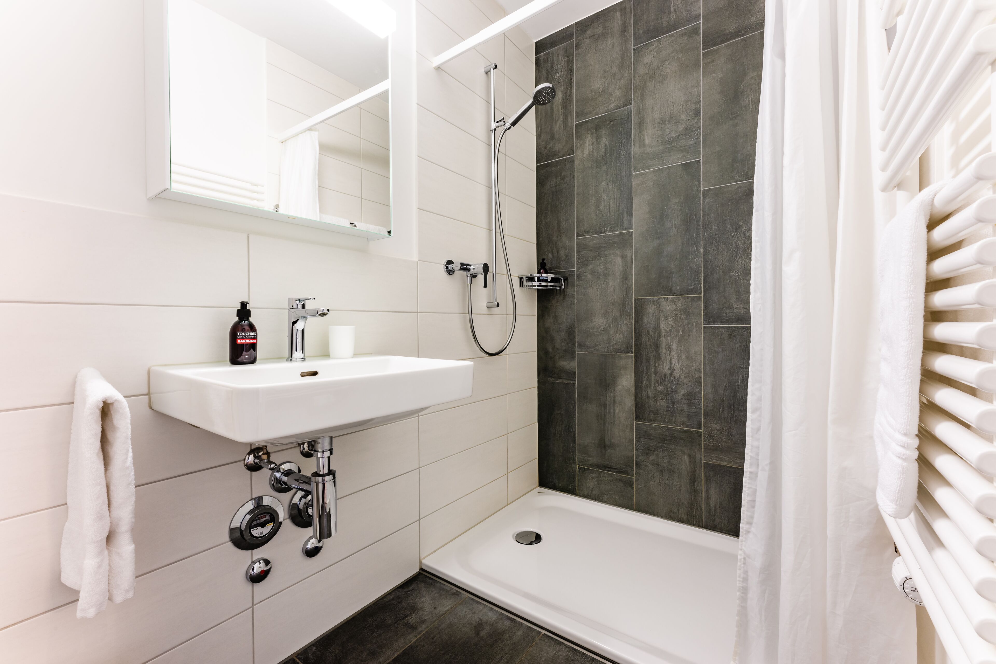 A modern bathroom with a white sink, mirror, and shower.