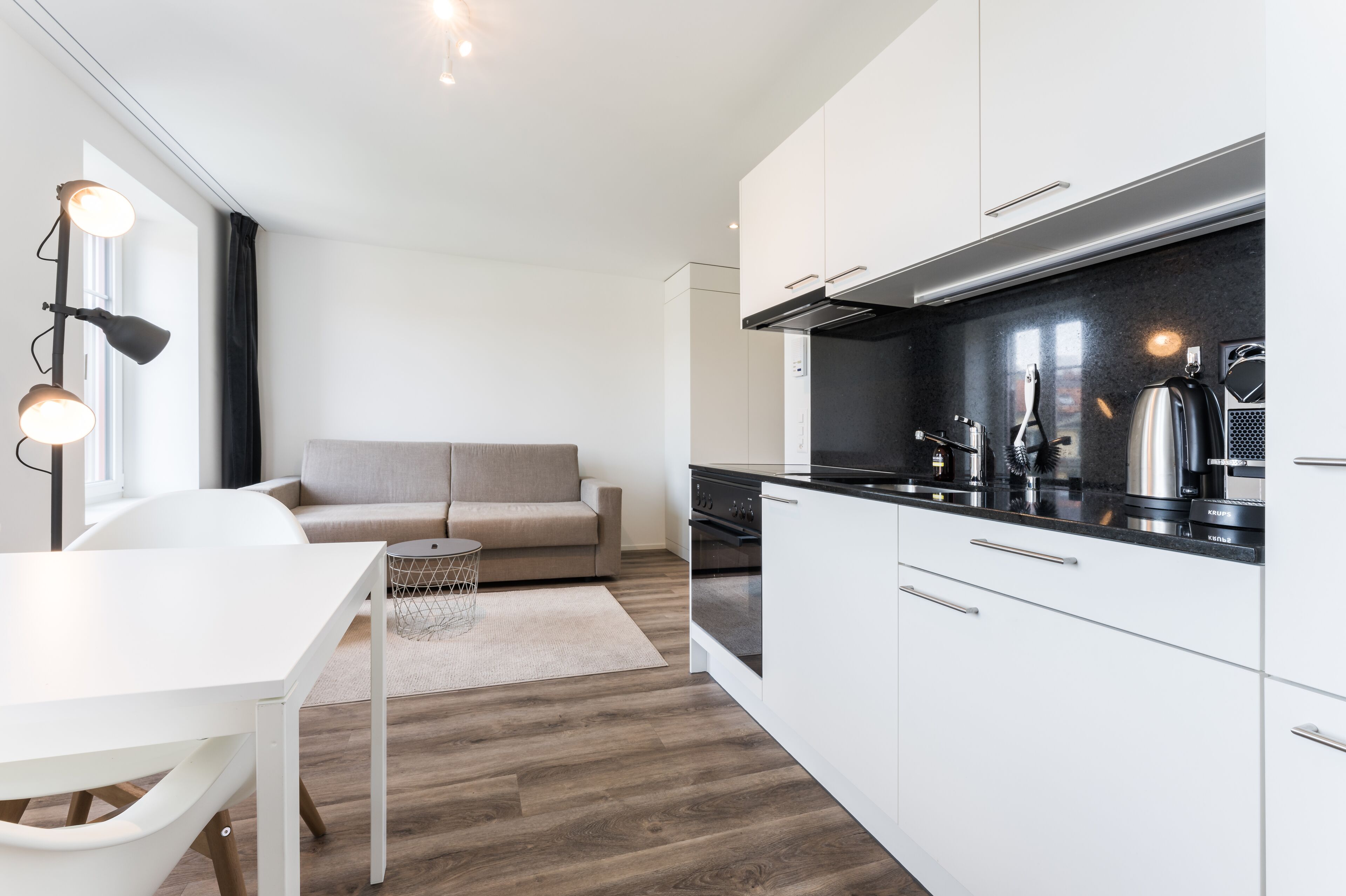 Una cocina moderna con armarios blancos, encimera negra y electrodomésticos de acero inoxidable.