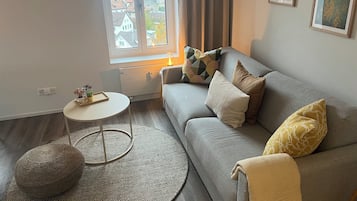Ein stilvolles Wohnzimmer mit grauem Sofa, einem runden Couchtisch, einem kleinen Beistelltisch und einem gewebten Ottomanen.