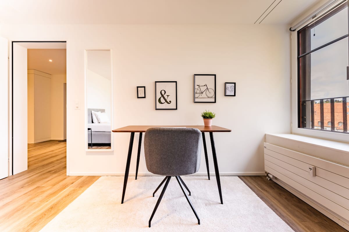 Habitació moderna amb terra de fusta, un radiador blanc, una finestra amb vistes i una taula amb una cadira.