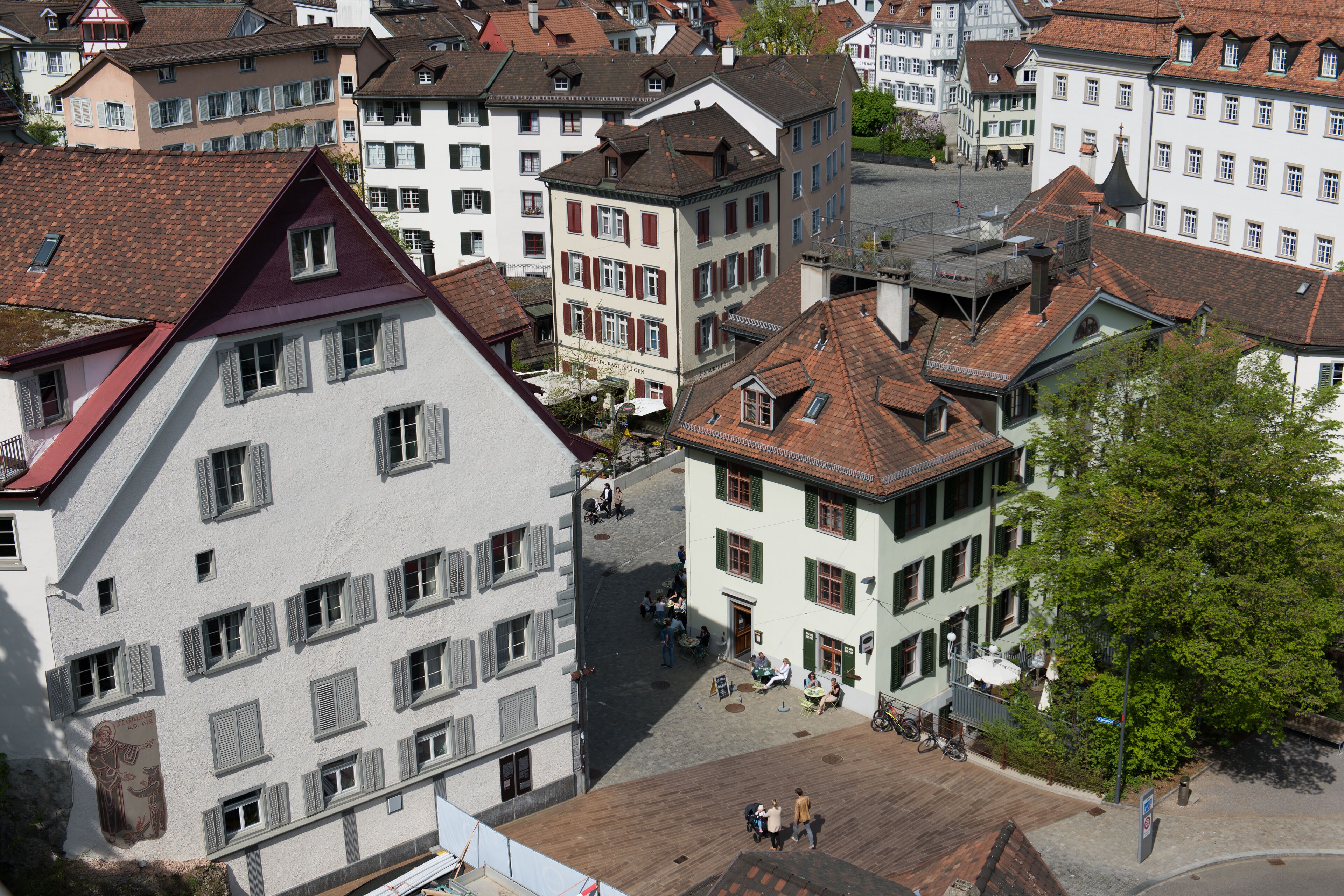A European town square with historic buildings, cobblestone streets, and outdoor seating areas.