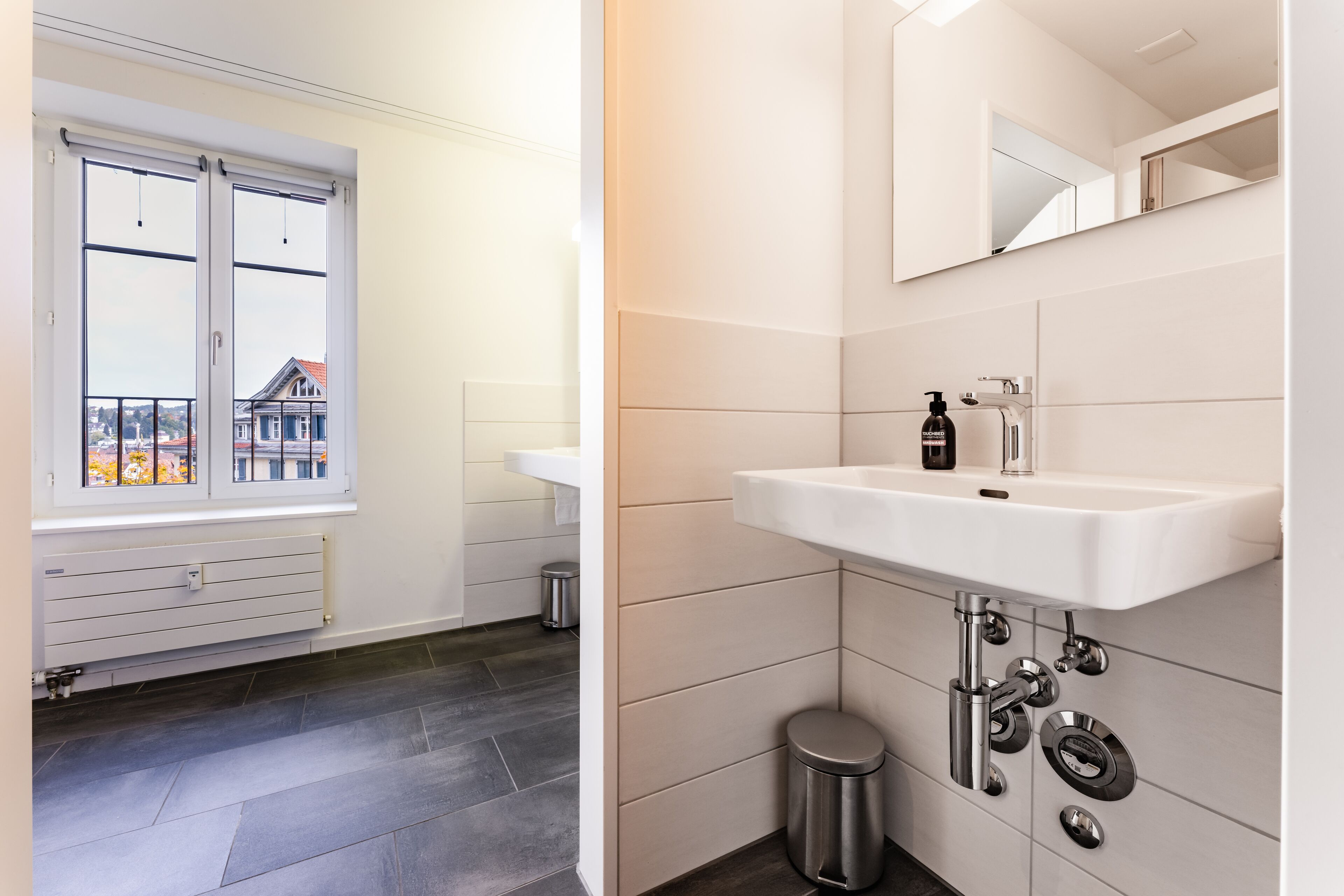 Ein modernes Badezimmer mit großem Fenster, einem weißen Waschbecken und einem Spiegel.