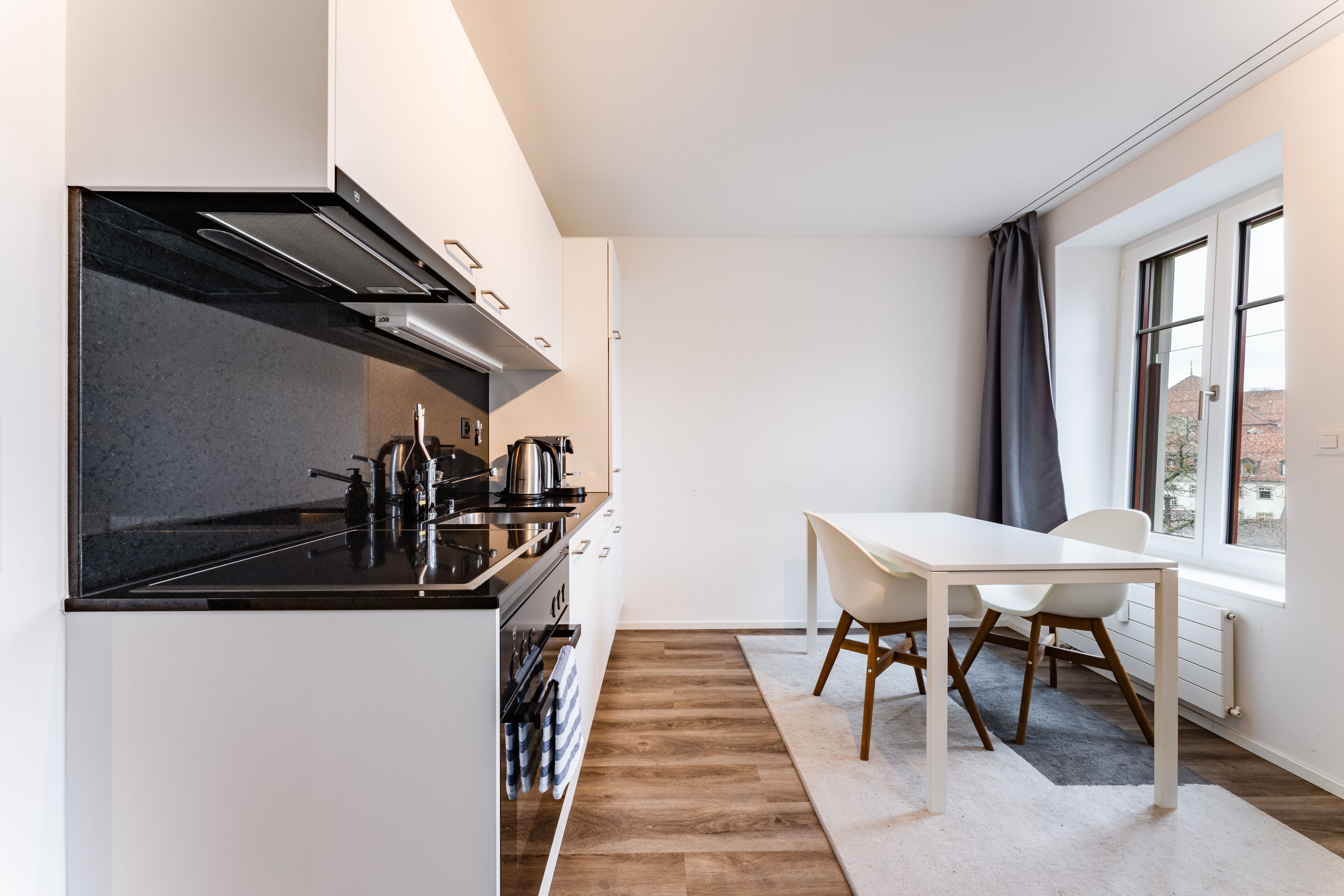 A modern kitchen with a black stove, white cabinets, and a dining area with a white table and chairs.