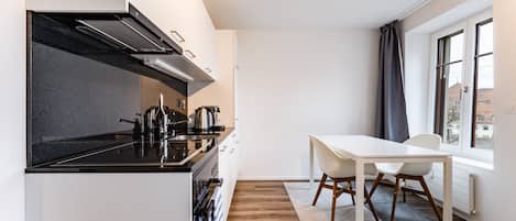 A modern kitchen with a black stove, white cabinets, and a dining area with a white table and chairs.