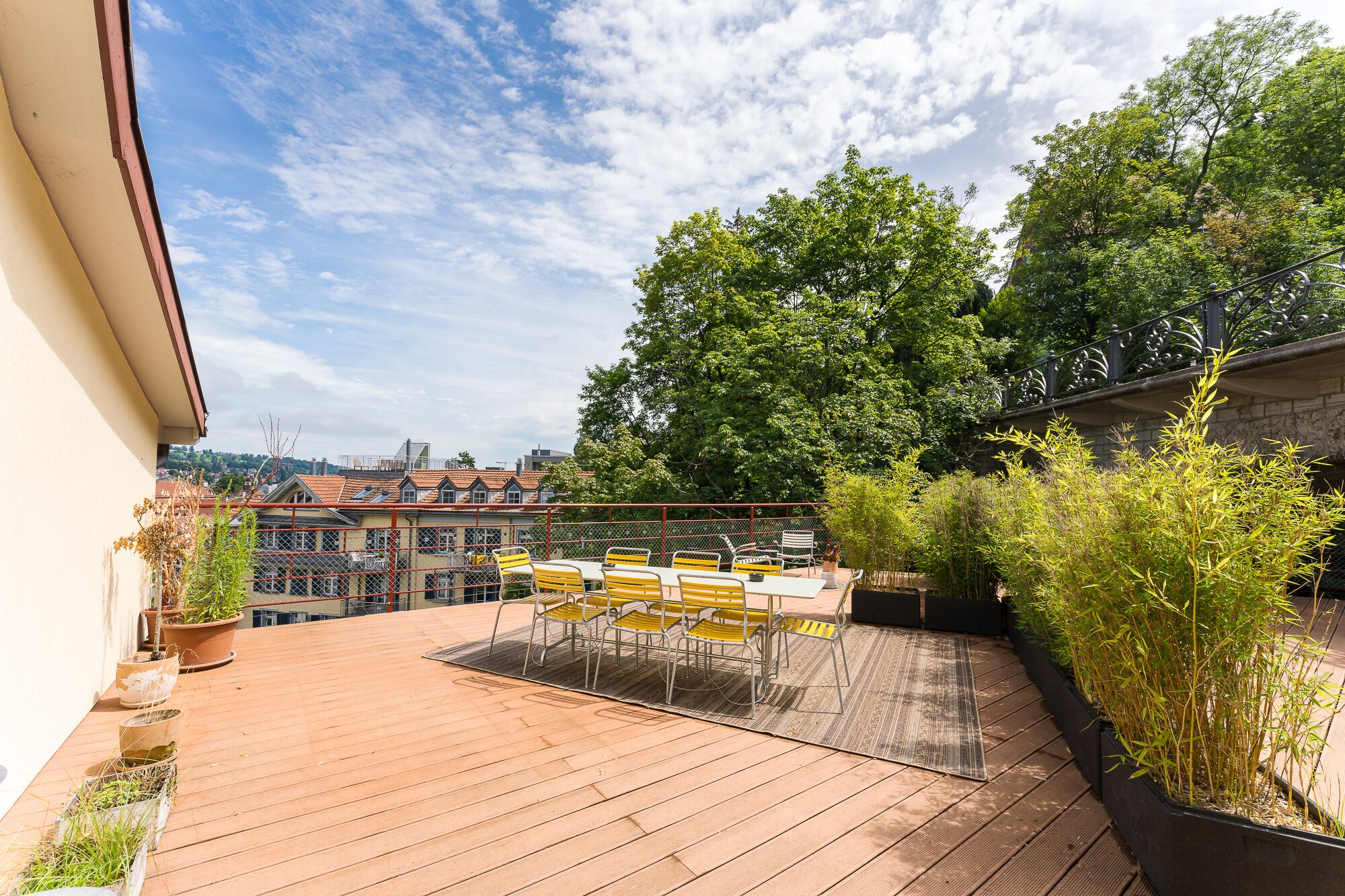 Une terrasse en bois, agréée de mobilier d’extérieur, entourée de verdure et avec une vue sur la ville en arrière-plan.