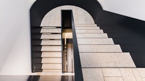Una escalera moderna con un arco negro y peldaños color beige que baja a un nivel inferior.