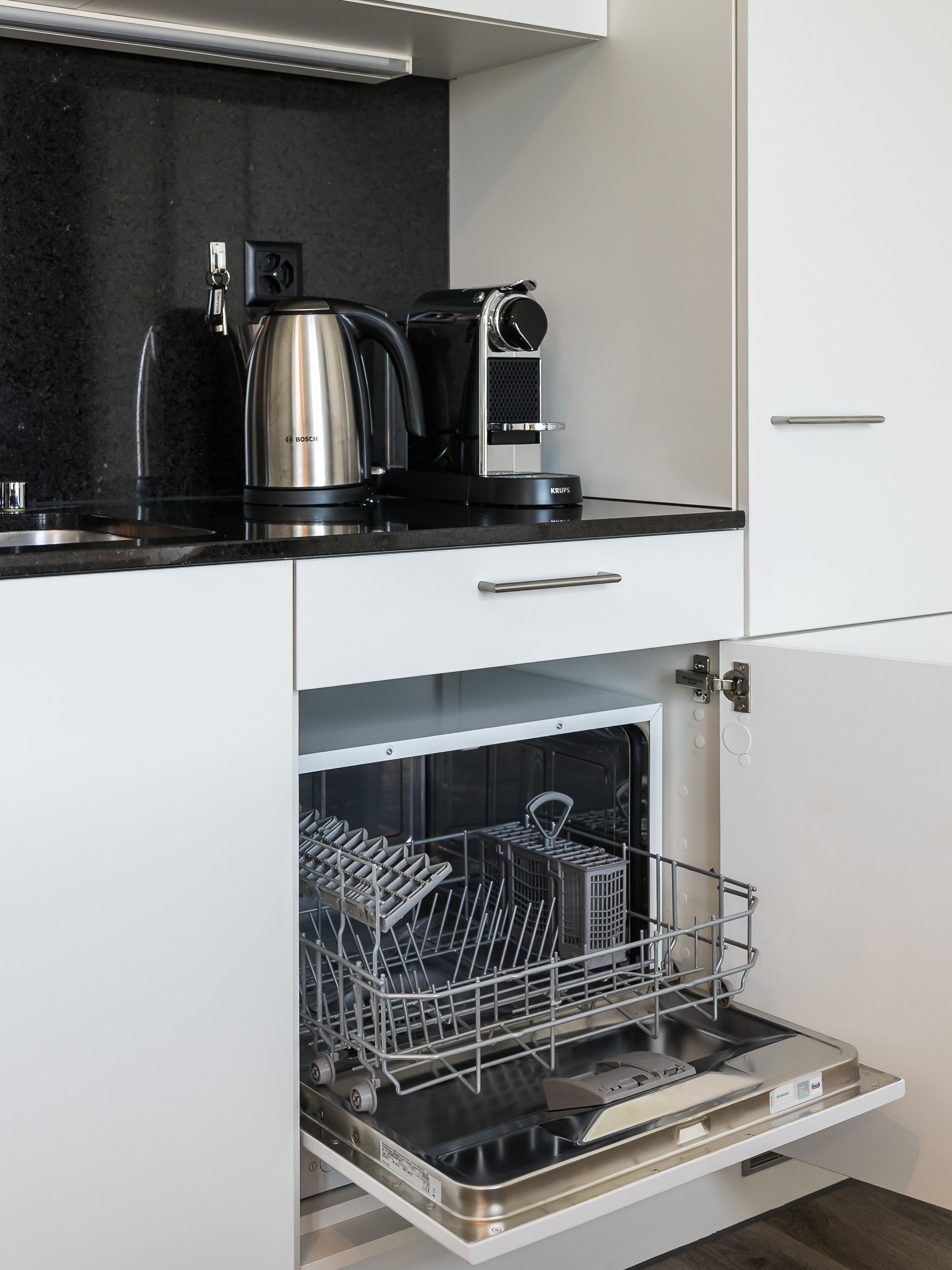 A modern kitchen with a Bosch coffee maker, a kettle, and a dishwasher with racks.