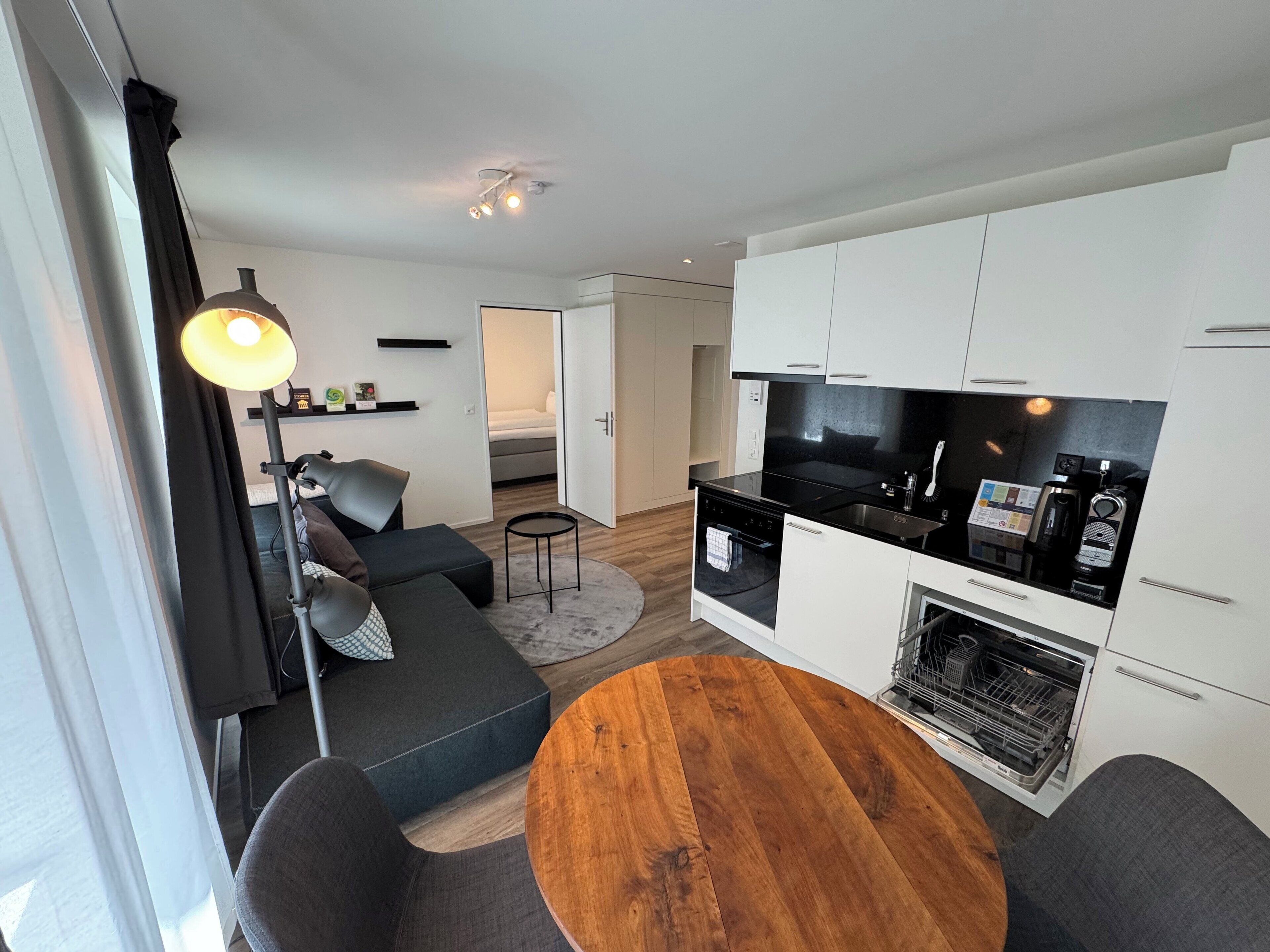 Un espace de vie moderne et compact comprenant un coin cuisine, un espace repas avec une table en bois et un canapé.