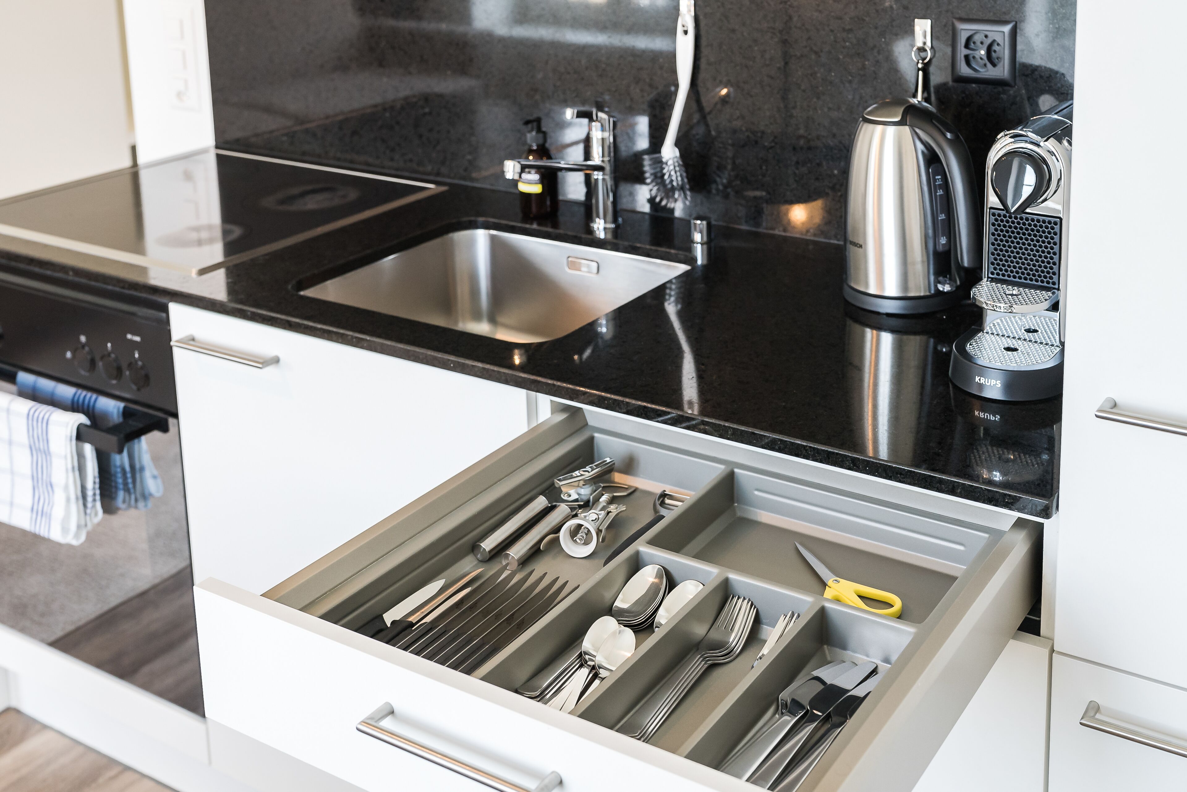 A kitchen with a black countertop, stainless steel sink, and a coffee maker.