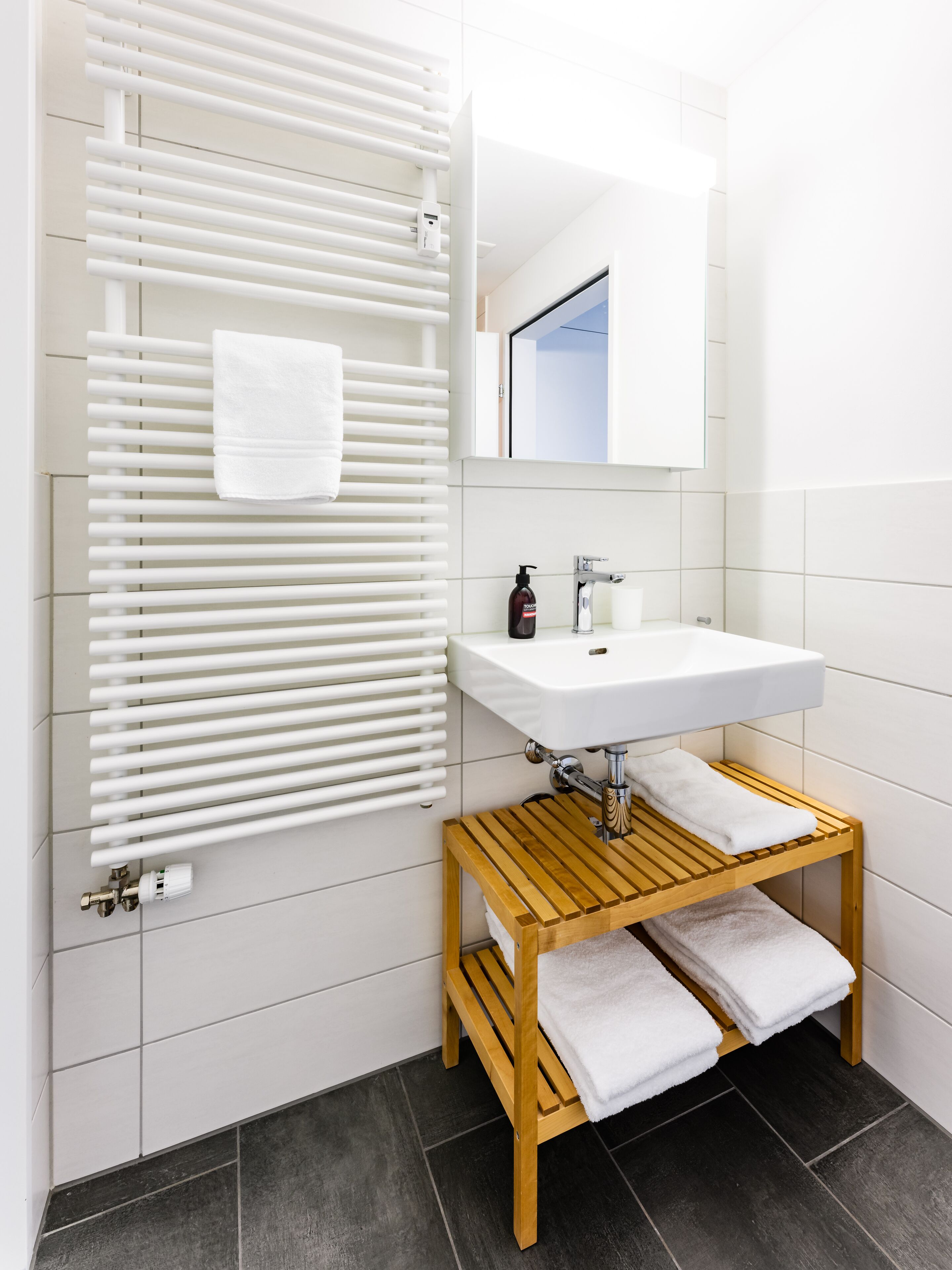 Ein modernes Badezimmer mit einem weißen Waschbecken, einem hölzernen Handtuchhalter und einem darauf liegenden Handtuch.