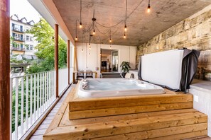Un bain à remous en bois sur un balcon, avec vue sur la verdure et les bâtiments.