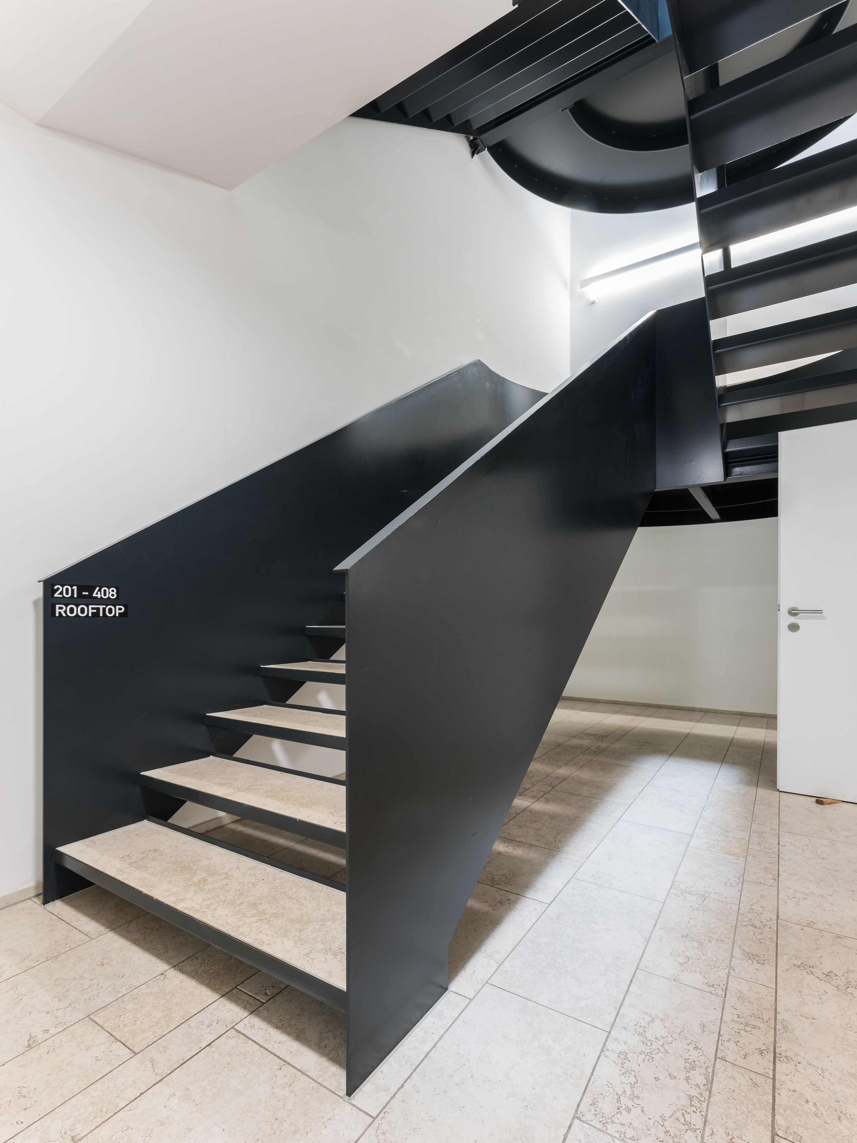 A modern staircase with a black metal railing, beige steps, and a white wall.