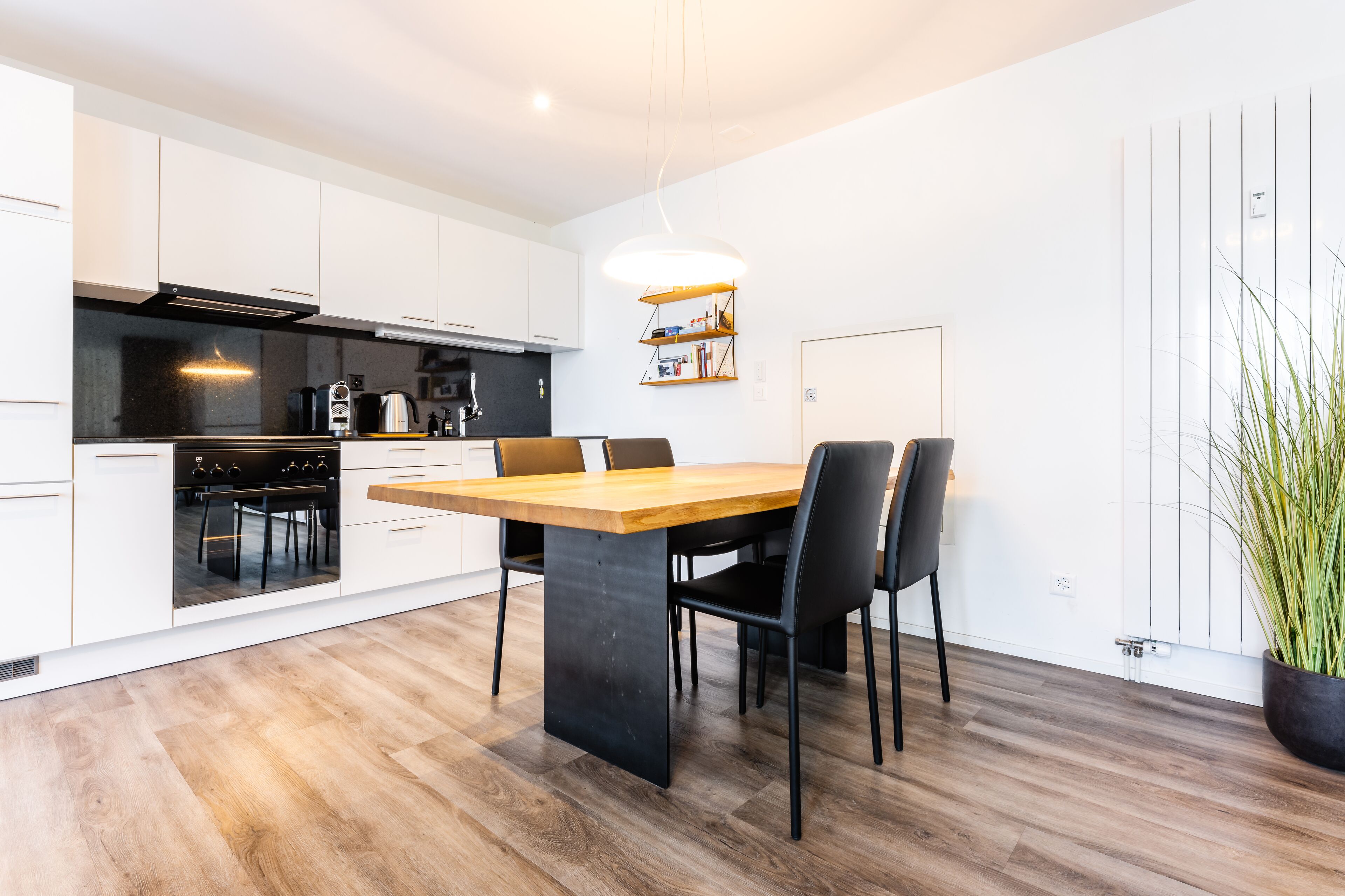 A modern kitchen with white cabinetry, a wooden dining table, and black chairs.