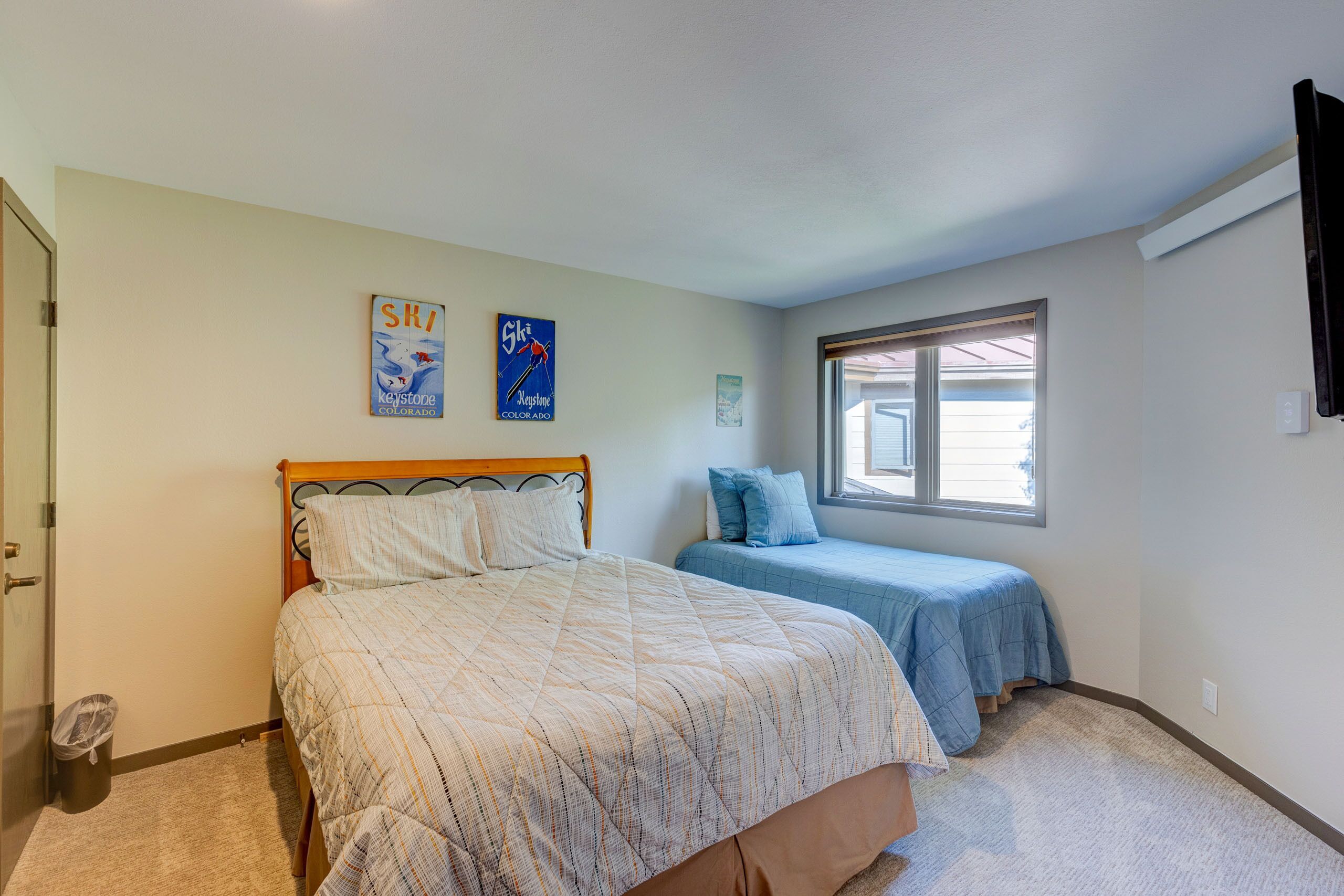 Une chambre avec un grand lit, un plus petit lit, une fenêtre et deux éléments de décoration murale.
