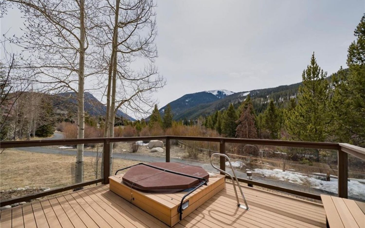 A wooden deck with a massage table and a chair, overlooking a river and mountains.