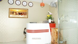 A reception area with a white reception desk, multiple wall clocks, a framed picture of horses, a potted plant, and a glass partition. - Trinh Ngoc Hotel (Ho Chi Minh City)