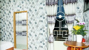 A hotel room with a hexagonal patterned wall, a wooden bed, a red sofa, a dining table with a vase of flowers, and curtains with a geometric design. - Trinh Ngoc Hotel (Ho Chi Minh City)