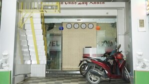 A hotel entrance with a staircase leading up to the door, a red scooter parked outside, and a sign with the hotel's name and contact information. - Trinh Ngoc Hotel (Ho Chi Minh City)