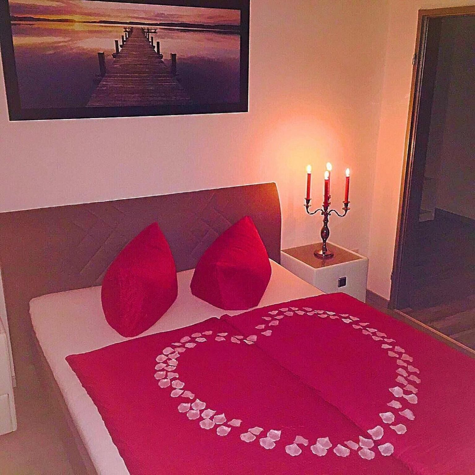 A bedroom with a bed, red pillows, a candelabra, and a framed picture on the wall.