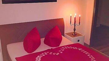 A bedroom with a bed, red pillows, a candelabra, and a framed picture on the wall.