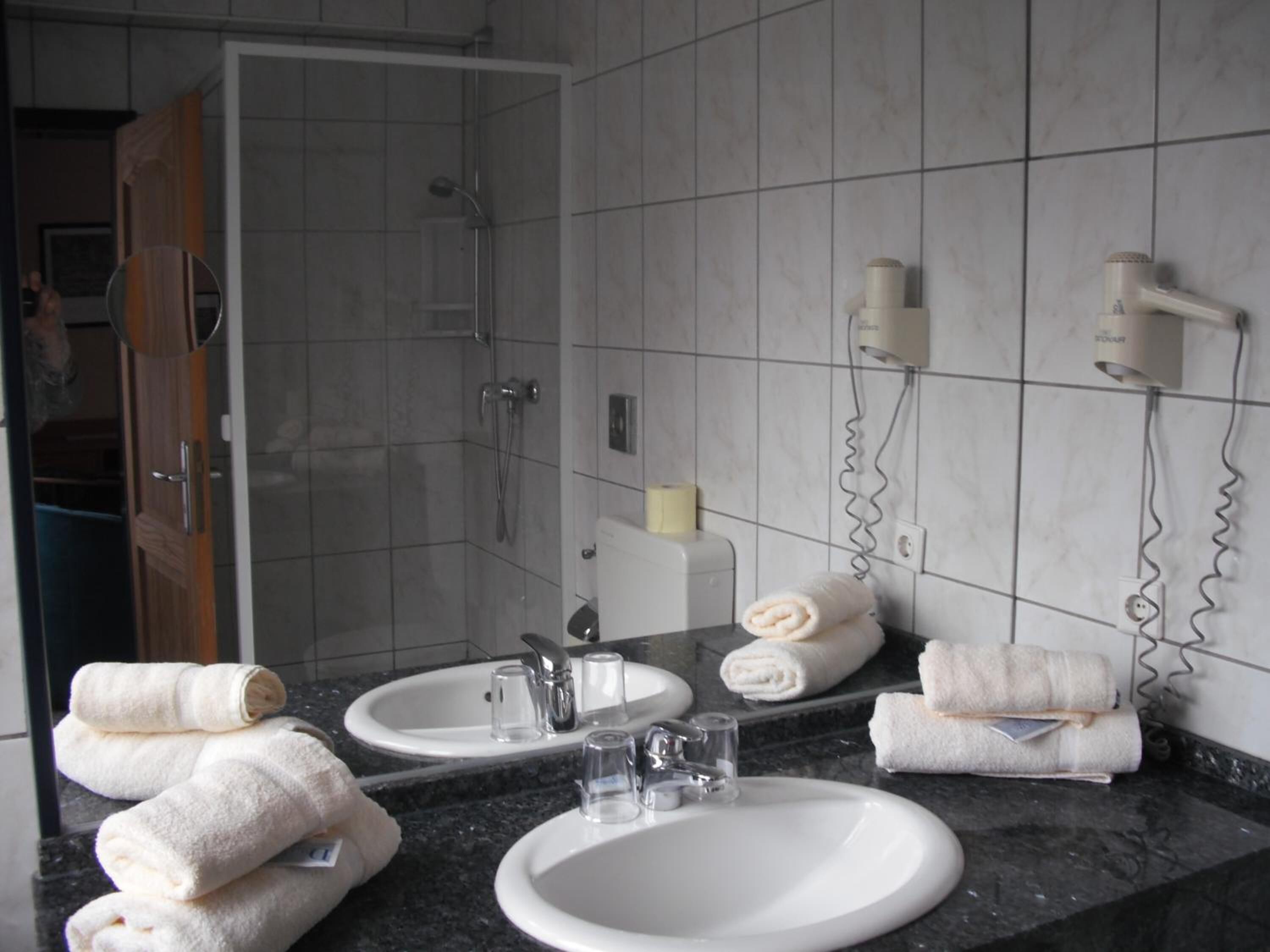 Een badkamer met twee wastafels, een douche en een spiegel. Op het aanrecht liggen handdoeken en een haardroger.