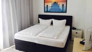 Habitació d'hotel amb un llit, una tauleta de nit, un escriptori i un ordinador.