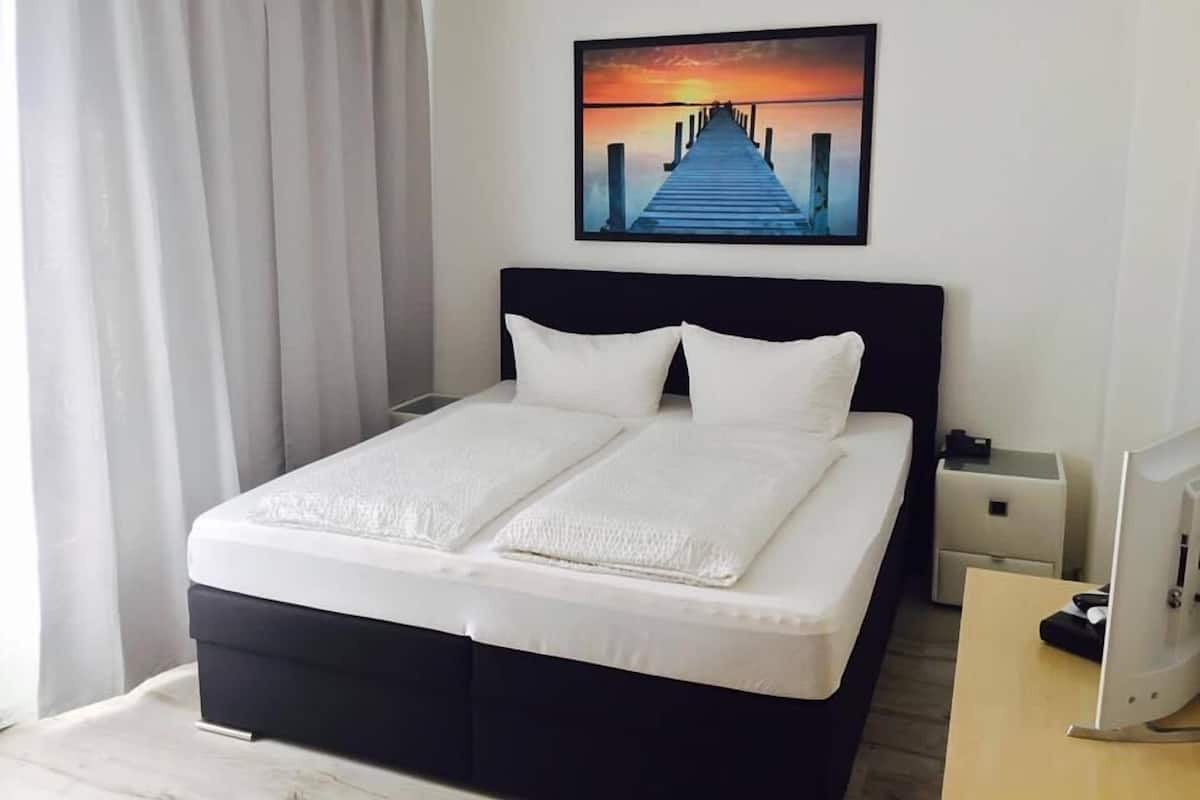 Una habitación de hotel con una cama, una mesita de noche, un escritorio y una computadora.