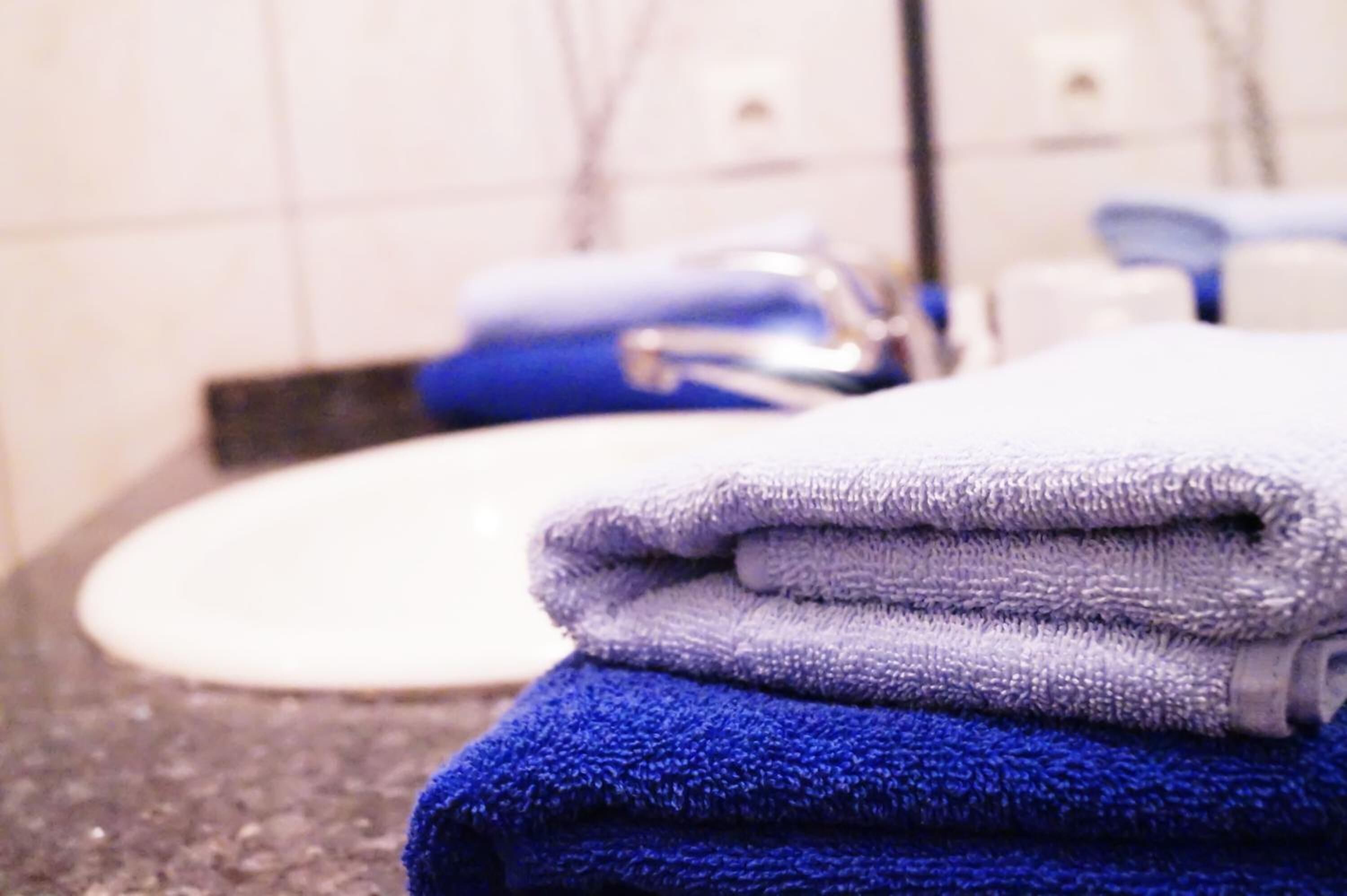 A bathroom with a sink and stacked towels in shades of blue and white.