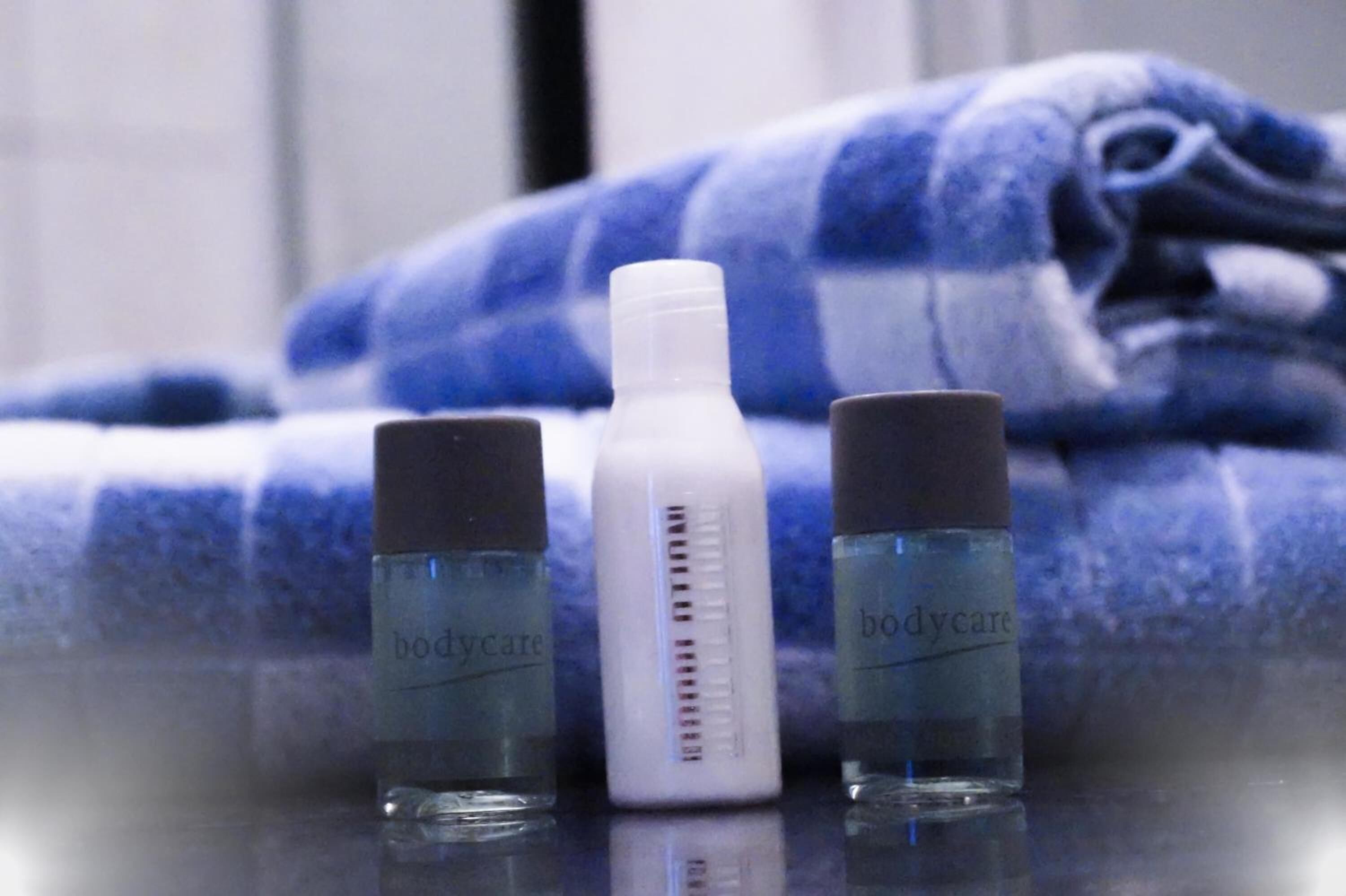 Three bottles of bodycare products on a reflective surface with a blue and white checkered towel in the background.