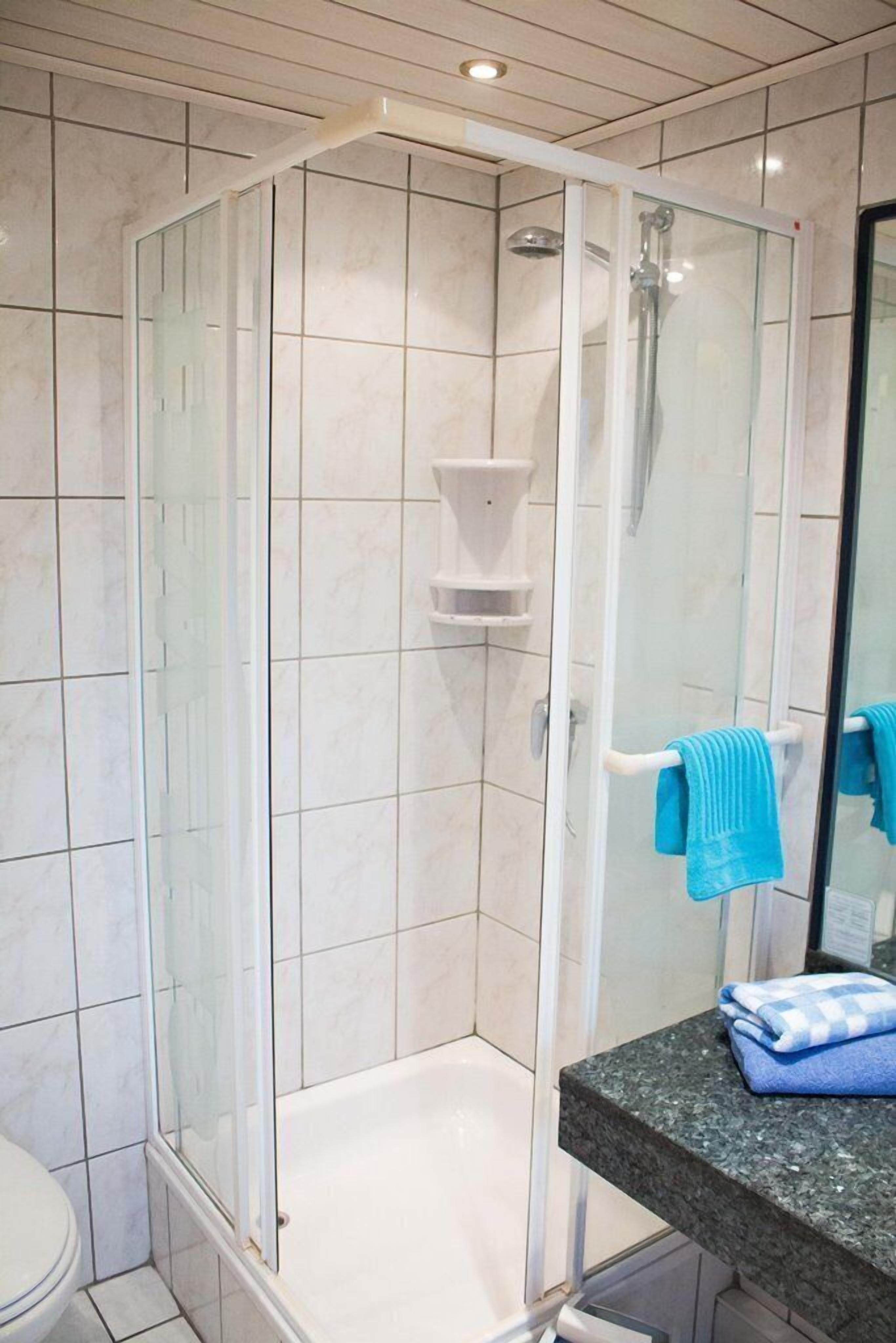 A bathroom with a glass-enclosed shower, a white bathtub, and a countertop with a towel.