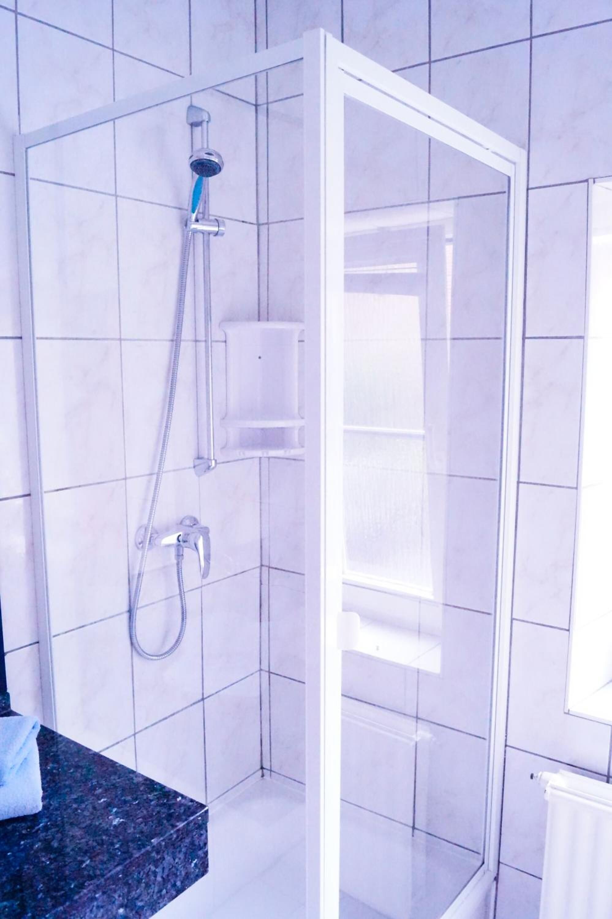 Eine Dusche mit Glastür, ein Handtuch auf der Ablagefläche und eine weiße Fliesenwand.
