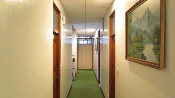 A hotel hallway with green carpet, wooden doors, and a framed landscape painting on the wall.