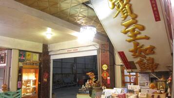 A traditional Chinese shop with a large golden sign, shelves with various items, and a brick wall entrance.