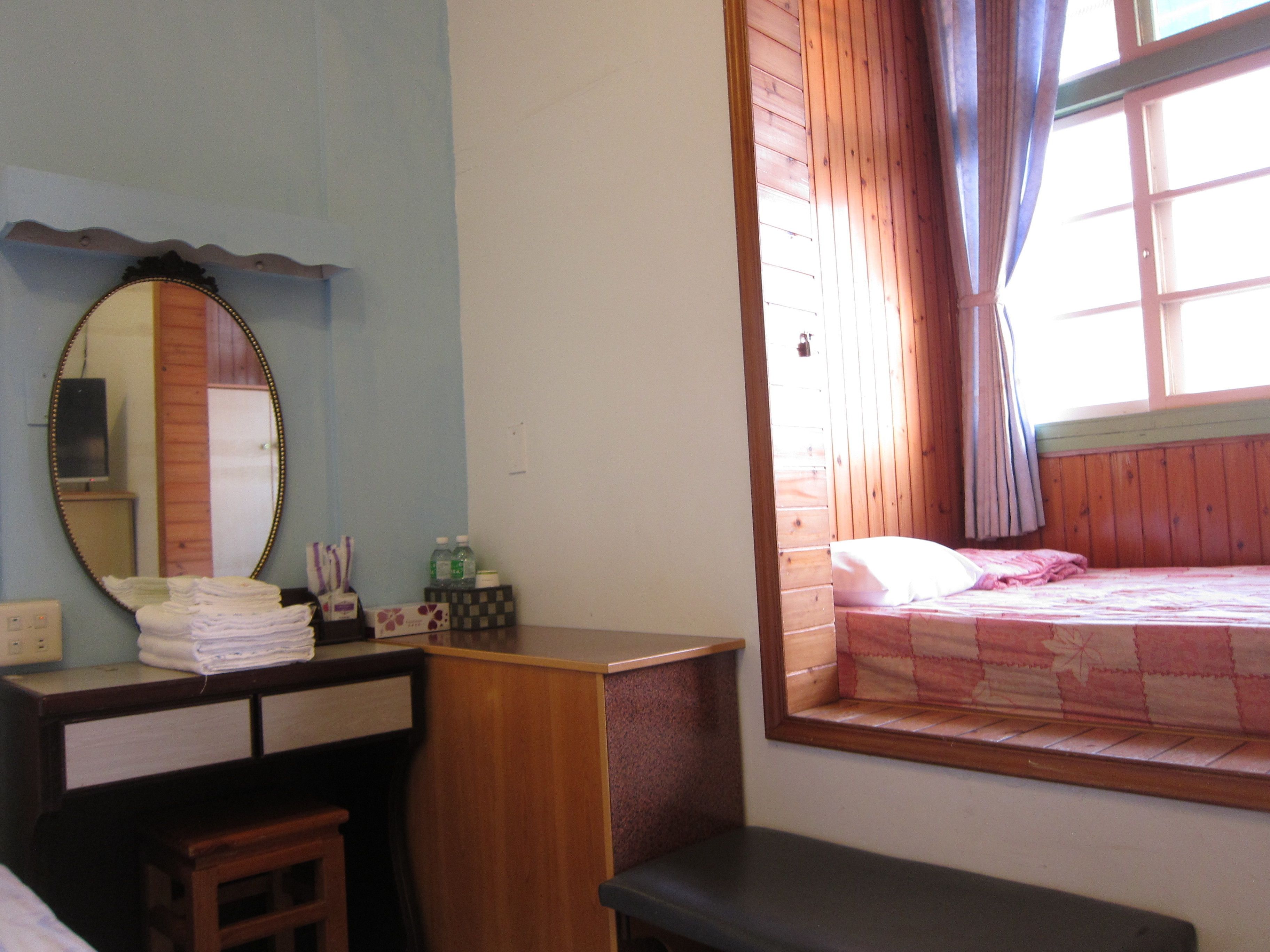 Une chambre à coucher avec un lit en bois, un petit bureau doté d’un miroir et une fenêtre avec des rideaux.
