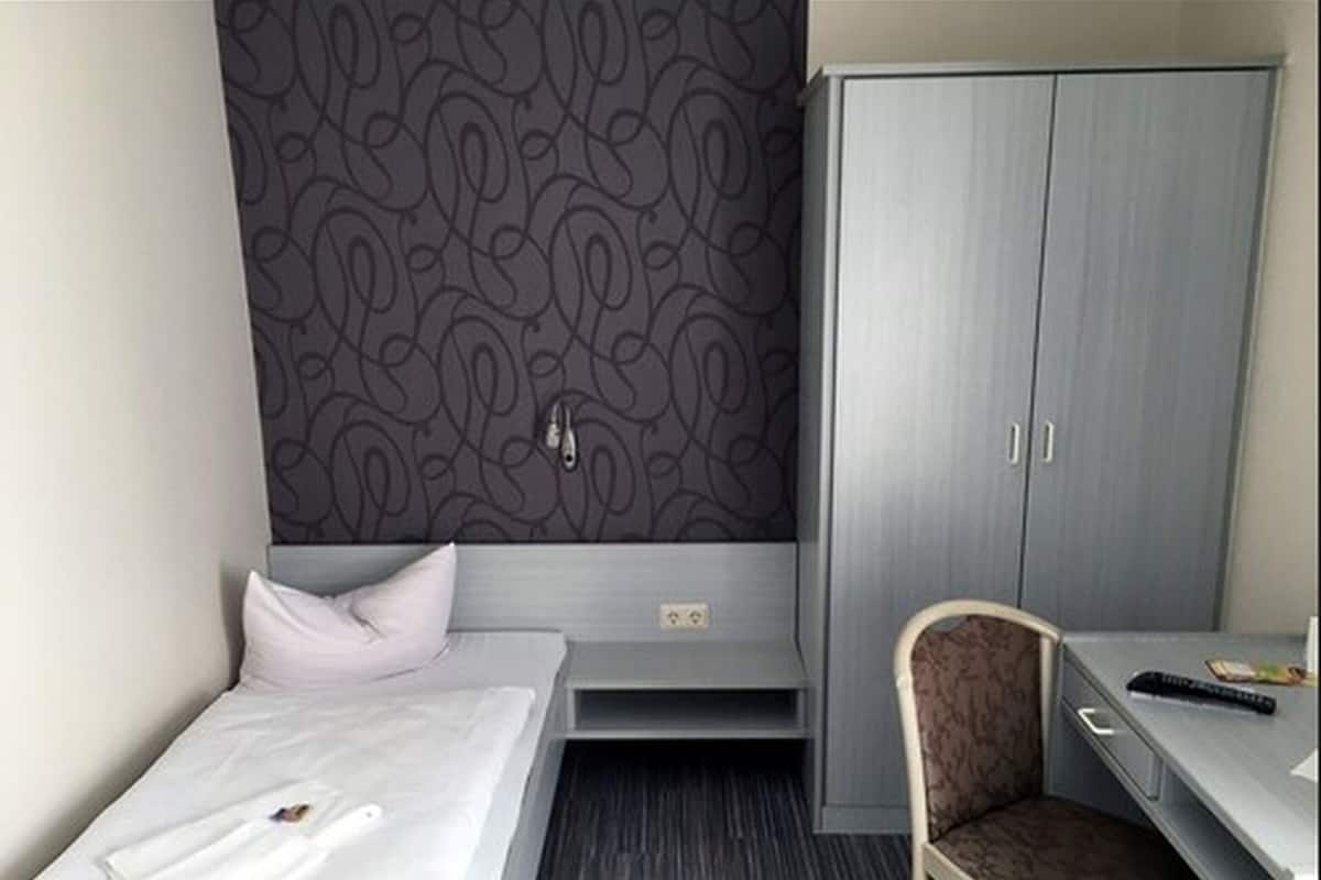 A hotel room with a bed, a desk, a chair, and a wardrobe.