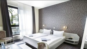 Habitación de hotel con una cama grande, un escritorio con silla, una mesa con una botella y una cuchara, y vista al exterior.