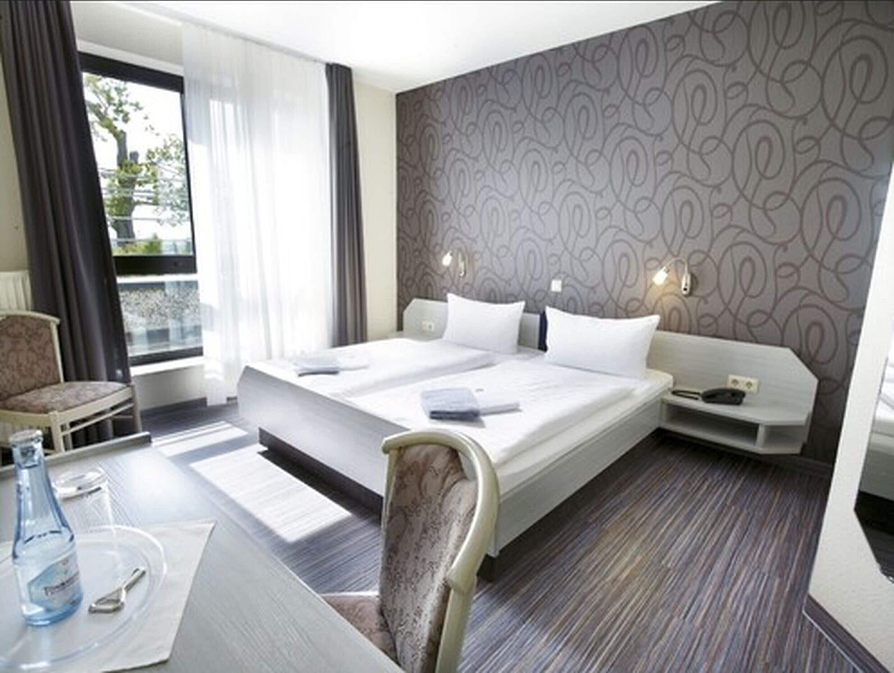 Een hotelkamer met een groot bed, een bureau met een stoel, een klein tafeltje met een fles en lepel, en uitzicht op de omgeving.